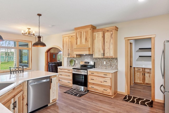 kitchen featuring appliances with stainless steel finishes, light brown cabinetry, decorative backsplash, light countertops, and arched walkways