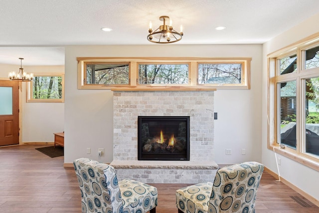 living area with a chandelier, wood finished floors, healthy amount of natural light, recessed lighting, and a brick fireplace