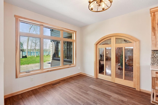 spare room featuring wood finished floors, a chandelier, and baseboards