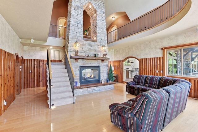living area with a high ceiling, arched walkways, wood finished floors, stairs, and a stone fireplace