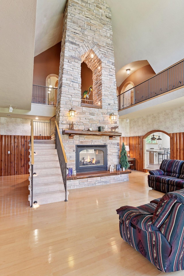living room with high vaulted ceiling, arched walkways, a fireplace, wood finished floors, and stairs