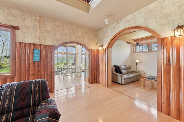 living area with arched walkways, healthy amount of natural light, wood finished floors, and a towering ceiling
