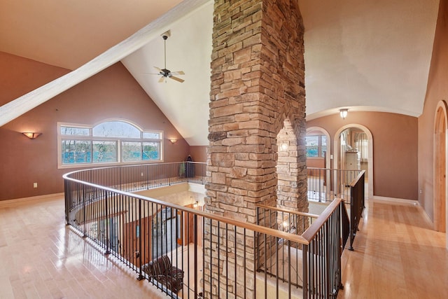 hallway featuring an upstairs landing, wood finished floors, arched walkways, baseboards, and high vaulted ceiling