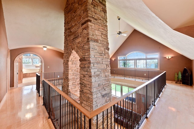 hallway with high vaulted ceiling, arched walkways, and an upstairs landing