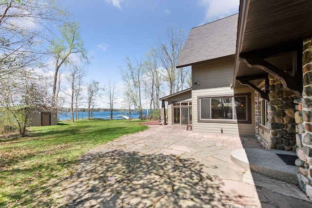 view of green lawn with a patio and a water view