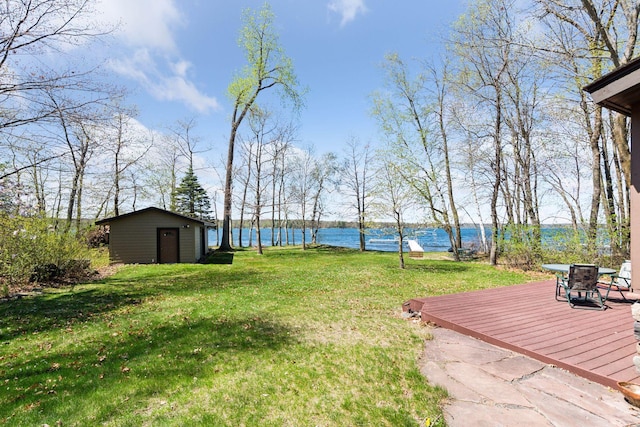 view of grassy yard with an outbuilding and a deck with water view