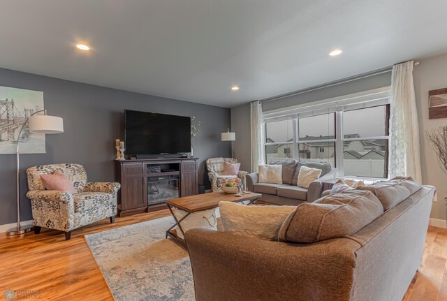 living area with light wood finished floors, recessed lighting, baseboards, and a glass covered fireplace