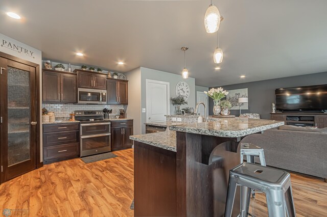 kitchen with stainless steel appliances, dark brown cabinets, a breakfast bar area, open floor plan, and light wood-type flooring