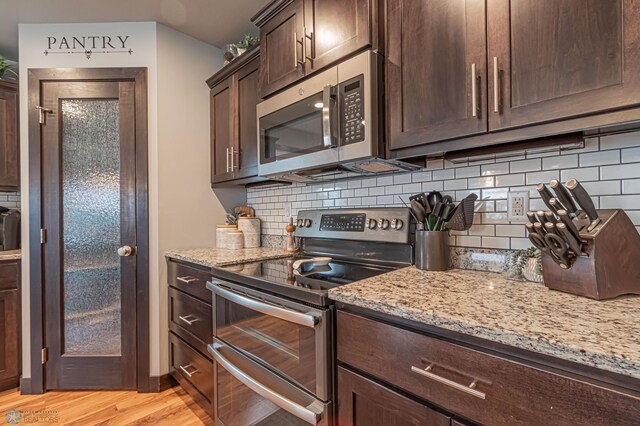 kitchen with appliances with stainless steel finishes, dark brown cabinetry, light stone countertops, light wood-style floors, and decorative backsplash
