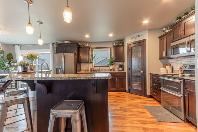 kitchen featuring appliances with stainless steel finishes, a breakfast bar area, tasteful backsplash, light wood finished floors, and recessed lighting
