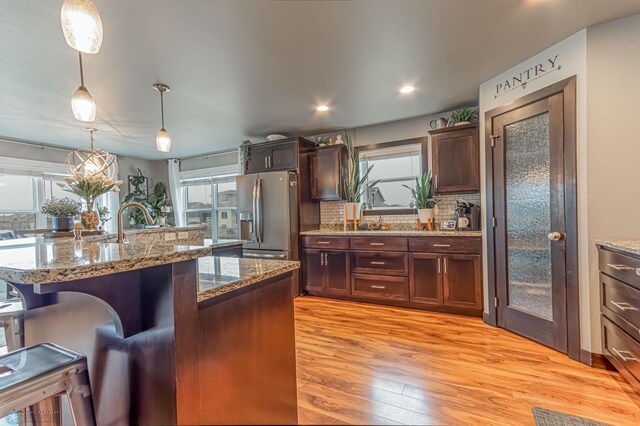 kitchen featuring stainless steel fridge with ice dispenser, a breakfast bar, light wood-style floors, pendant lighting, and tasteful backsplash