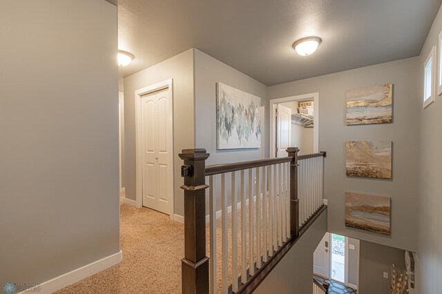 hallway with an upstairs landing, baseboards, healthy amount of natural light, and light carpet