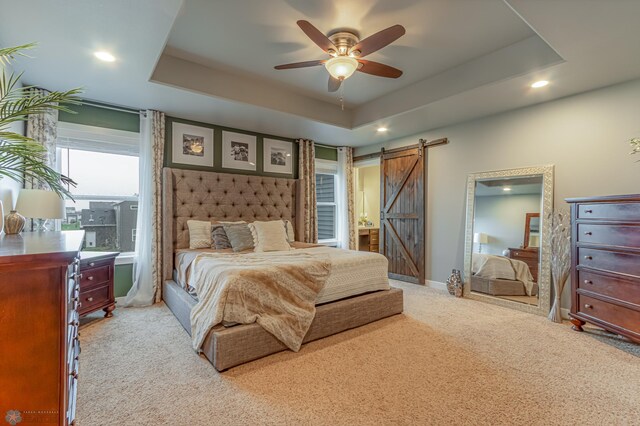 carpeted bedroom with a barn door, a raised ceiling, recessed lighting, baseboards, and ceiling fan