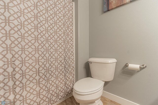 bathroom featuring baseboards, toilet, and a shower with curtain