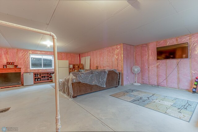 bedroom with concrete flooring, freestanding refrigerator, and fridge