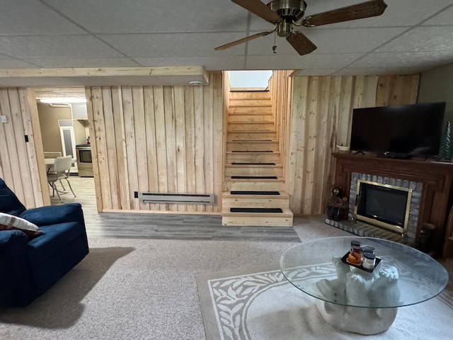 23479 State 200, Itasca Twp, MN 56676 - carpeted living room featuring wood walls, a brick fireplace, a drop ceiling, a ceiling fan, and stairs