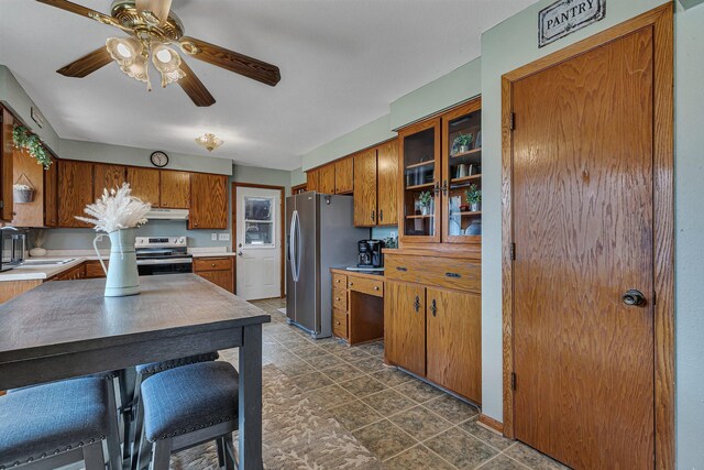 kitchen featuring appliances with stainless steel finishes, brown cabinetry, ceiling fan, and light countertops