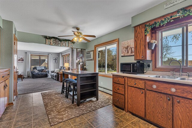 kitchen featuring a sink, black microwave, baseboard heating, a ceiling fan, and brown cabinetry