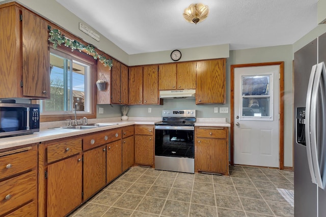 kitchen with stainless steel appliances, under cabinet range hood, a sink, and brown cabinetry