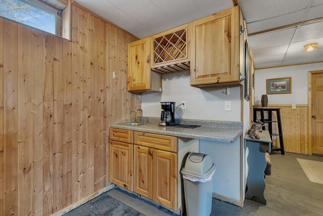kitchen featuring wood walls, a sink, light countertops, and concrete flooring