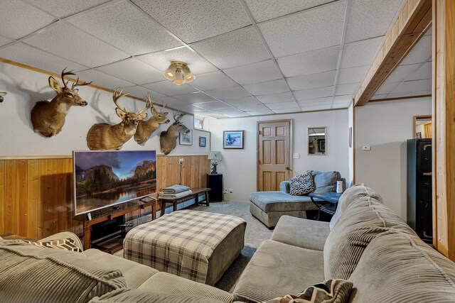 carpeted living room with wood walls, a paneled ceiling, and a wainscoted wall