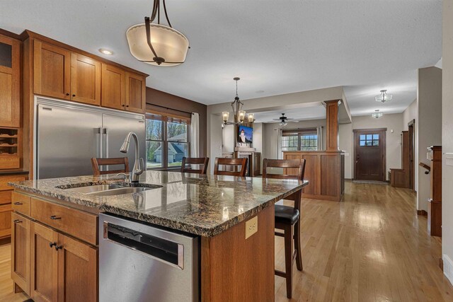 1901 11th St N, Sartell, MN 56377 - kitchen with stainless steel appliances, a sink, brown cabinets, a kitchen breakfast bar, and light wood-type flooring