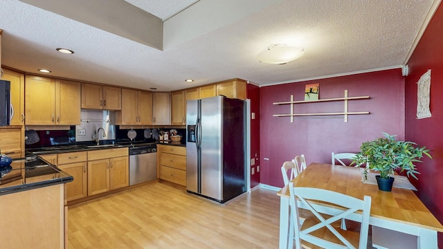 kitchen featuring appliances with stainless steel finishes, a textured ceiling, light wood-type flooring, dark countertops, and a sink