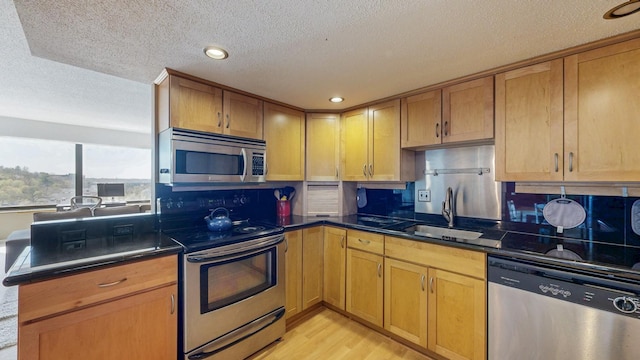 kitchen with stainless steel appliances, a sink, a textured ceiling, dark countertops, and light wood-style floors