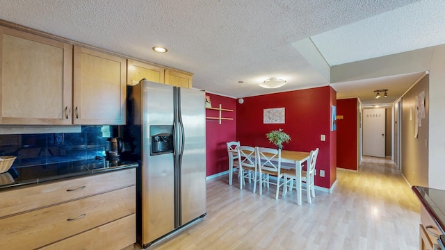 kitchen with stainless steel fridge, light wood-type flooring, light brown cabinetry, dark countertops, and a textured ceiling