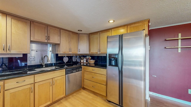 kitchen with stainless steel appliances, a sink, light wood-style flooring, backsplash, and a textured ceiling