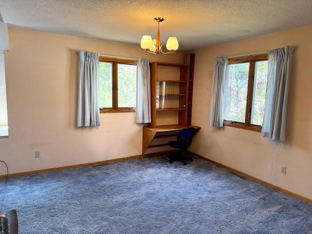 empty room featuring a chandelier, plenty of natural light, a textured ceiling, carpet flooring, and baseboards