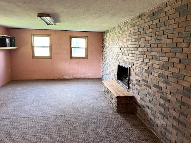 unfurnished living room with brick wall, a brick fireplace, a textured ceiling, and carpet floors