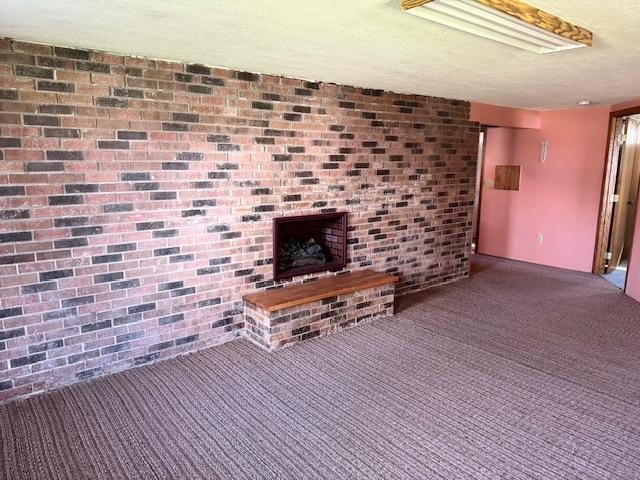 unfurnished living room with carpet, a brick fireplace, a textured ceiling, and brick wall