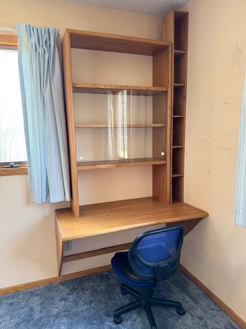 unfurnished office with carpet floors, built in desk, and baseboards