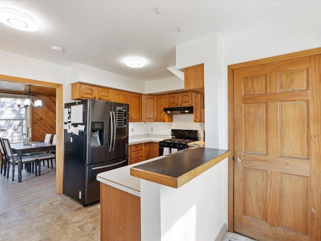 kitchen with refrigerator with ice dispenser, black gas range oven, under cabinet range hood, a peninsula, and brown cabinets