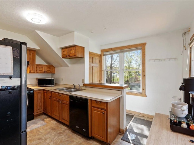 kitchen featuring black appliances, a sink, light countertops, brown cabinetry, and a peninsula