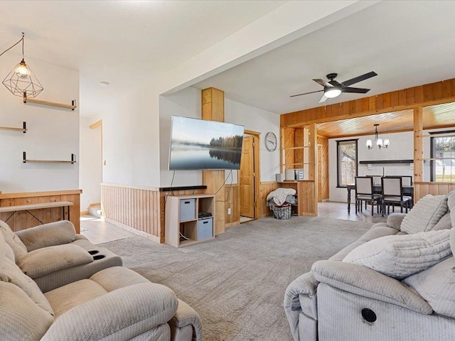 carpeted living area featuring wooden walls, a chandelier, a ceiling fan, and a wainscoted wall