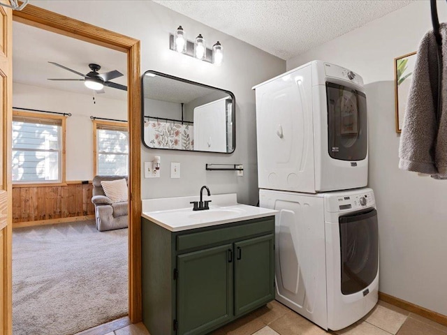 clothes washing area with cabinet space, stacked washer / dryer, a textured ceiling, a ceiling fan, and wainscoting