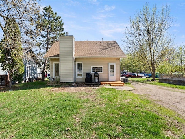rear view of house featuring a chimney, a yard, driveway, cooling unit, and roof with shingles