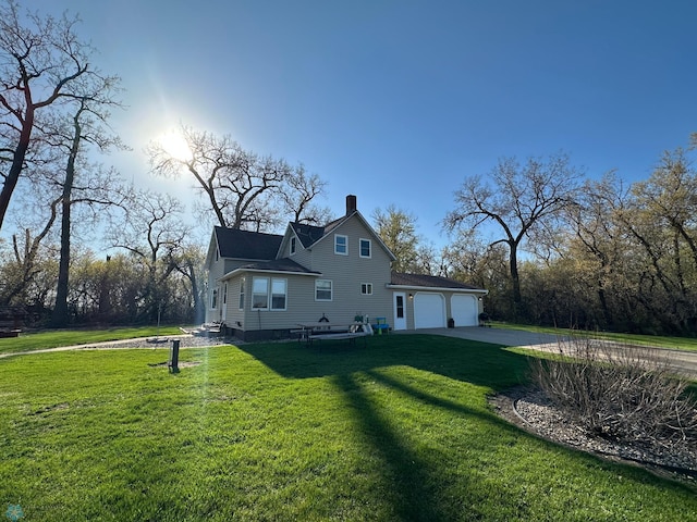 back of house with an attached garage, a yard, driveway, and a chimney