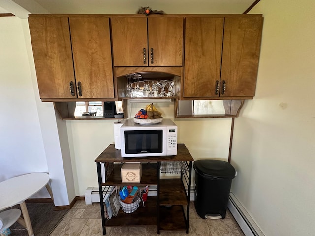 kitchen featuring white microwave, brown cabinetry, baseboards, and a baseboard heating unit