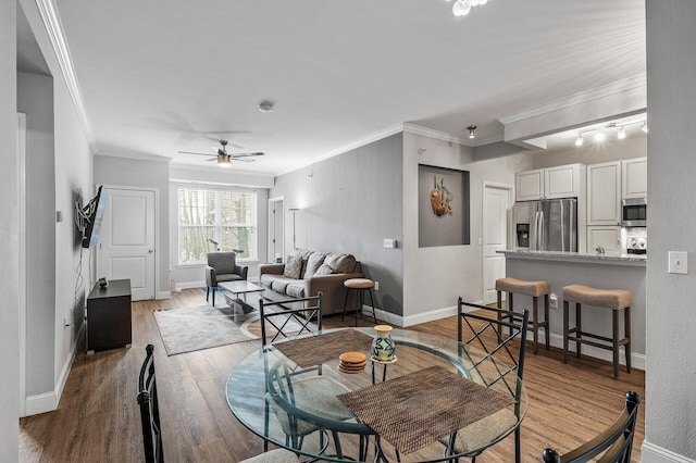 dining room with crown molding, ceiling fan, wood finished floors, and baseboards
