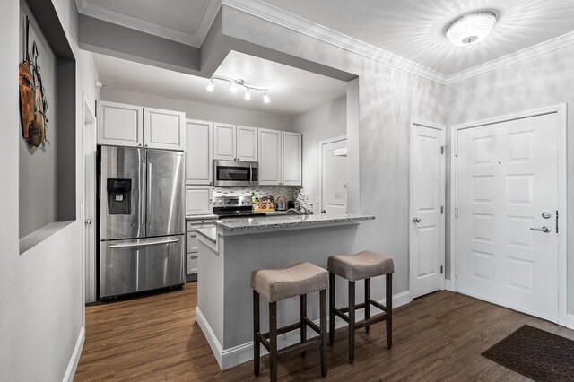 kitchen featuring stainless steel appliances, dark wood-type flooring, a breakfast bar area, light stone counters, and crown molding