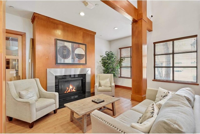 living room featuring light wood finished floors, a fireplace with flush hearth, recessed lighting, baseboards, and ornate columns