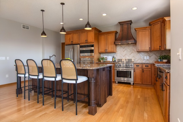 532 150th St, Alden Twp, WI 54001 - kitchen featuring appliances with stainless steel finishes, custom exhaust hood, light wood-type flooring, decorative backsplash, and brown cabinetry