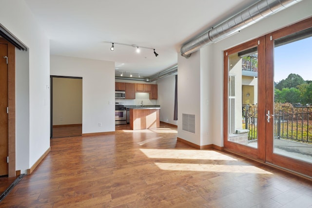unfurnished living room featuring wood finished floors, baseboards, and track lighting