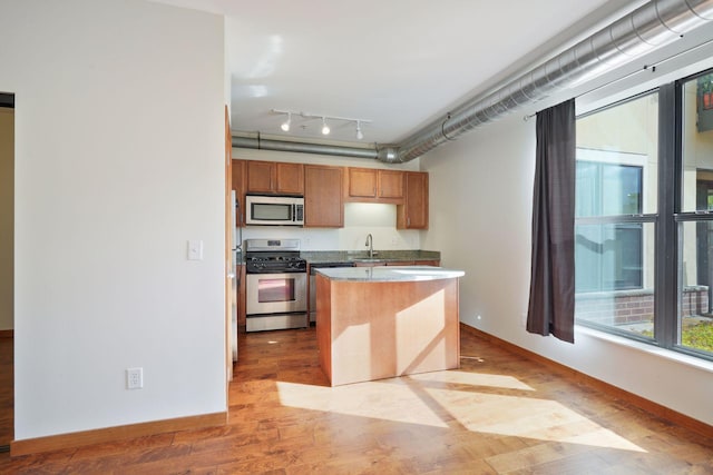 kitchen featuring stainless steel appliances, a sink, light wood-style flooring, and baseboards