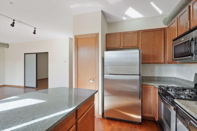 kitchen featuring stainless steel appliances, dark wood finished floors, stone countertops, brown cabinetry, and rail lighting