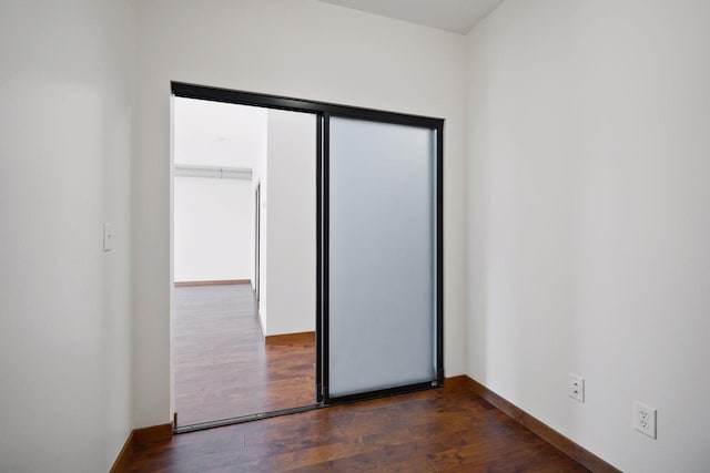 unfurnished bedroom with baseboards, dark wood-style floors, and a closet
