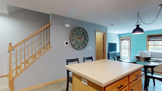 kitchen with a kitchen breakfast bar, brown cabinets, hanging light fixtures, a kitchen island, and a textured ceiling